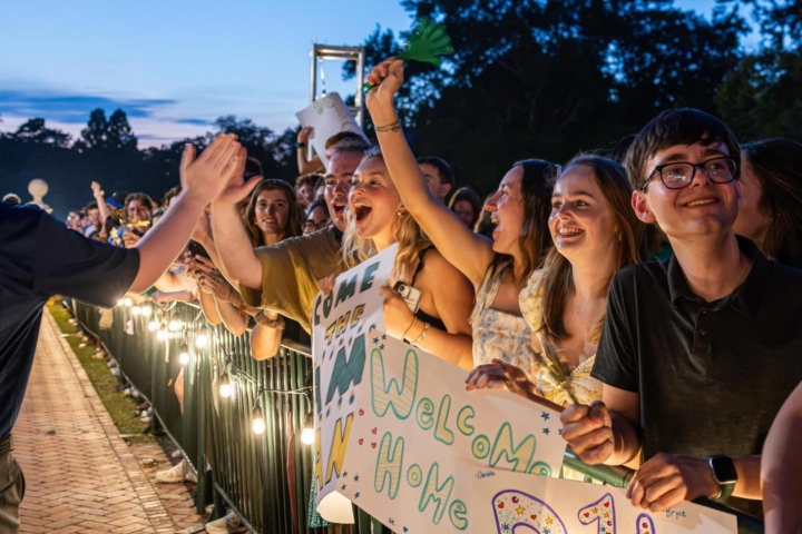 Returning students wave signs and trade high fives as new students walk through the Wren building for opening convocation.