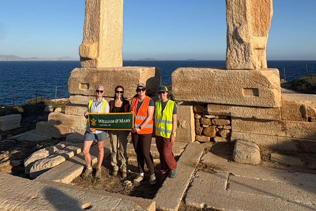 This is a photo of a W&M research team — Jess Paga, Maya Parfitt, Phoebe Kirsh, and Paige Martin — standing in front of the unfinished temple on Palatia, an islet off the coast of the Greek island Naxos.