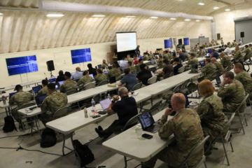People in military uniforms sit at tables in rows.