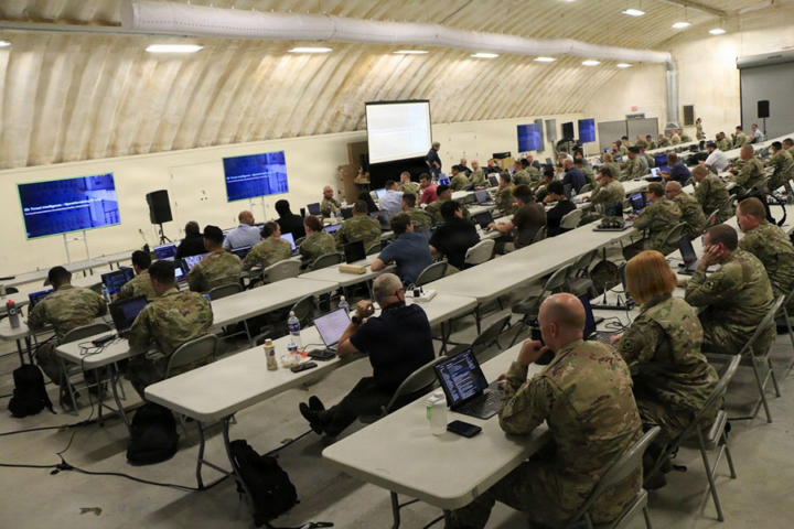 People in military uniforms sit at tables in rows.