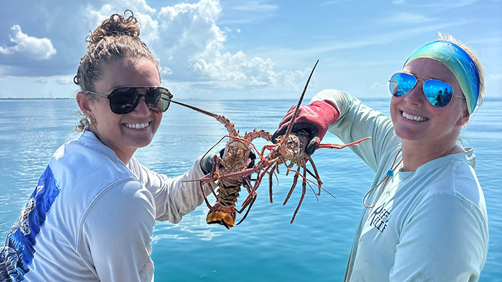 Two people hold up lobsters.