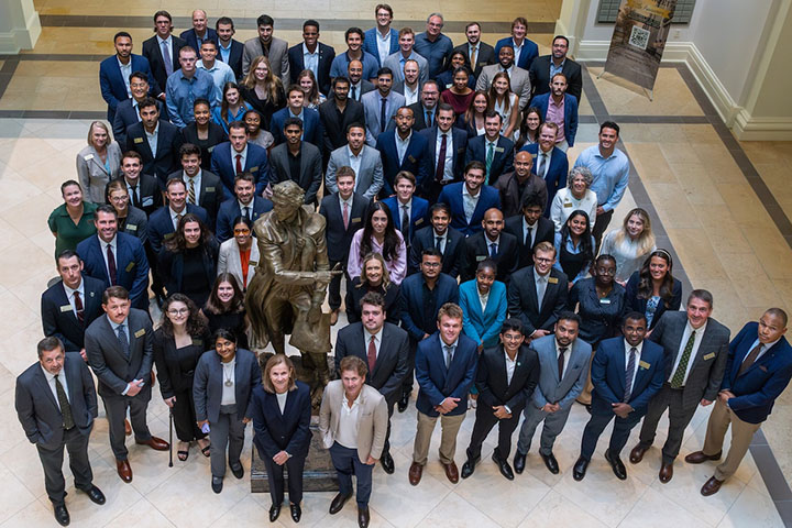 A large group of people in suits pose for a photo by a bronze statue.