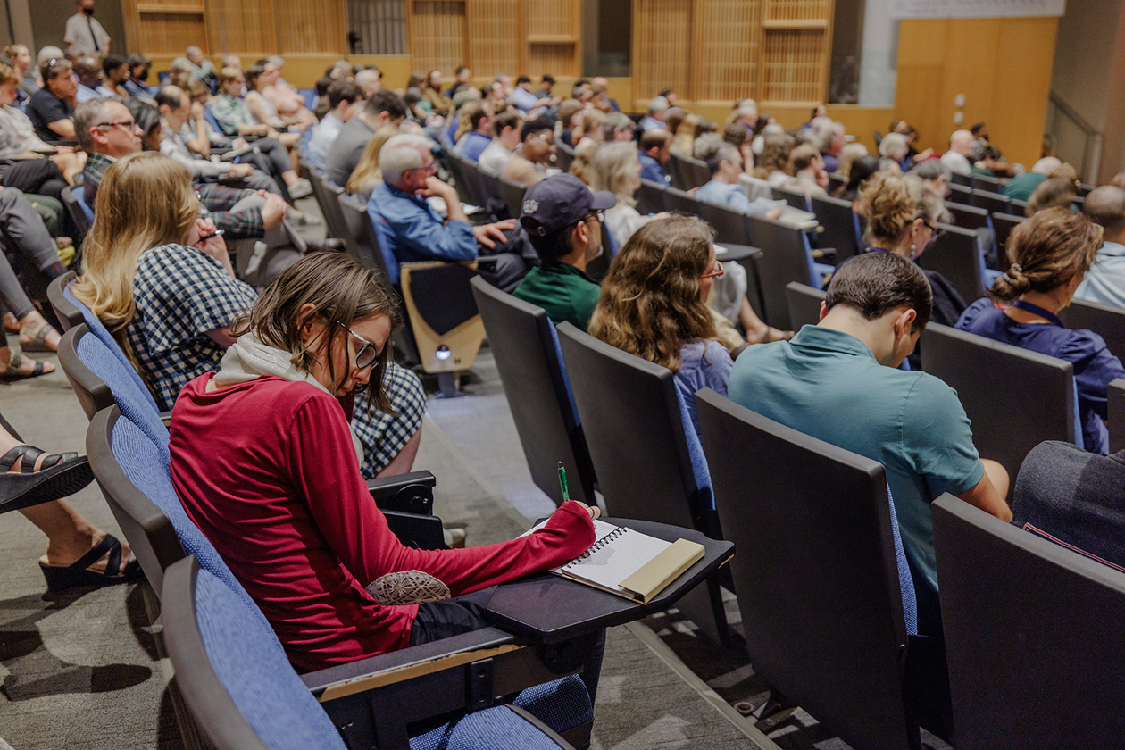 People sit in chairs in an auditorium and take notes.
