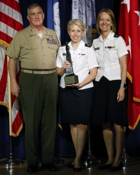Three people in military uniforms take a photo together next to flags.