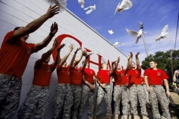 people in military pants and red shirts release doves.