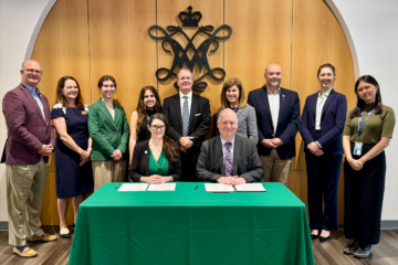 Two people sit at a table while others stand behind them.