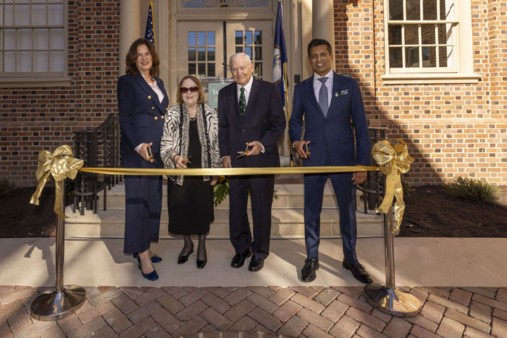 Four people prepare to cut a large, gold ribbon.