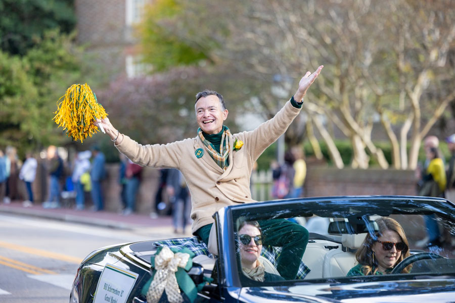 A person ride on the back of a convertible and waves a pom-pom.