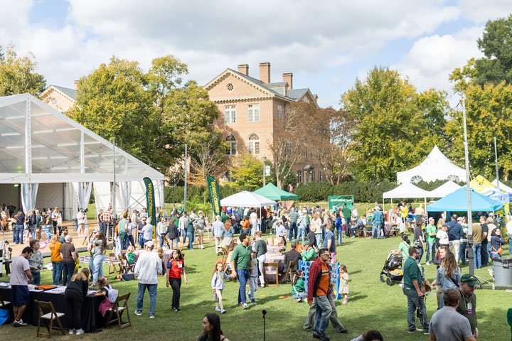 People gather in an outdoor location near a tent and brick building.