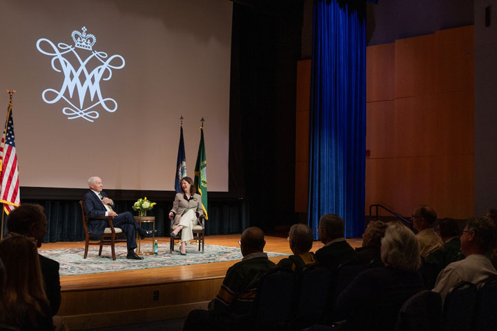 Two people speak on a stage in front of an audience.