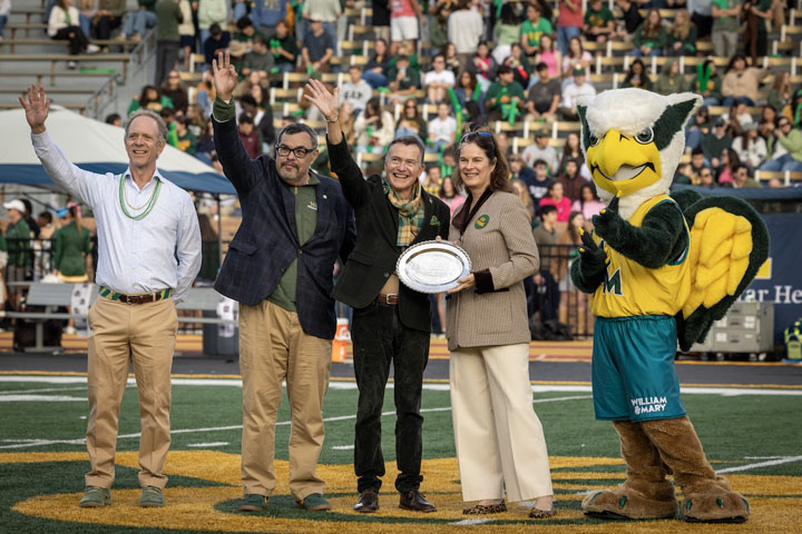 People pose for a photo while standing on a football field and hold a silver tray.